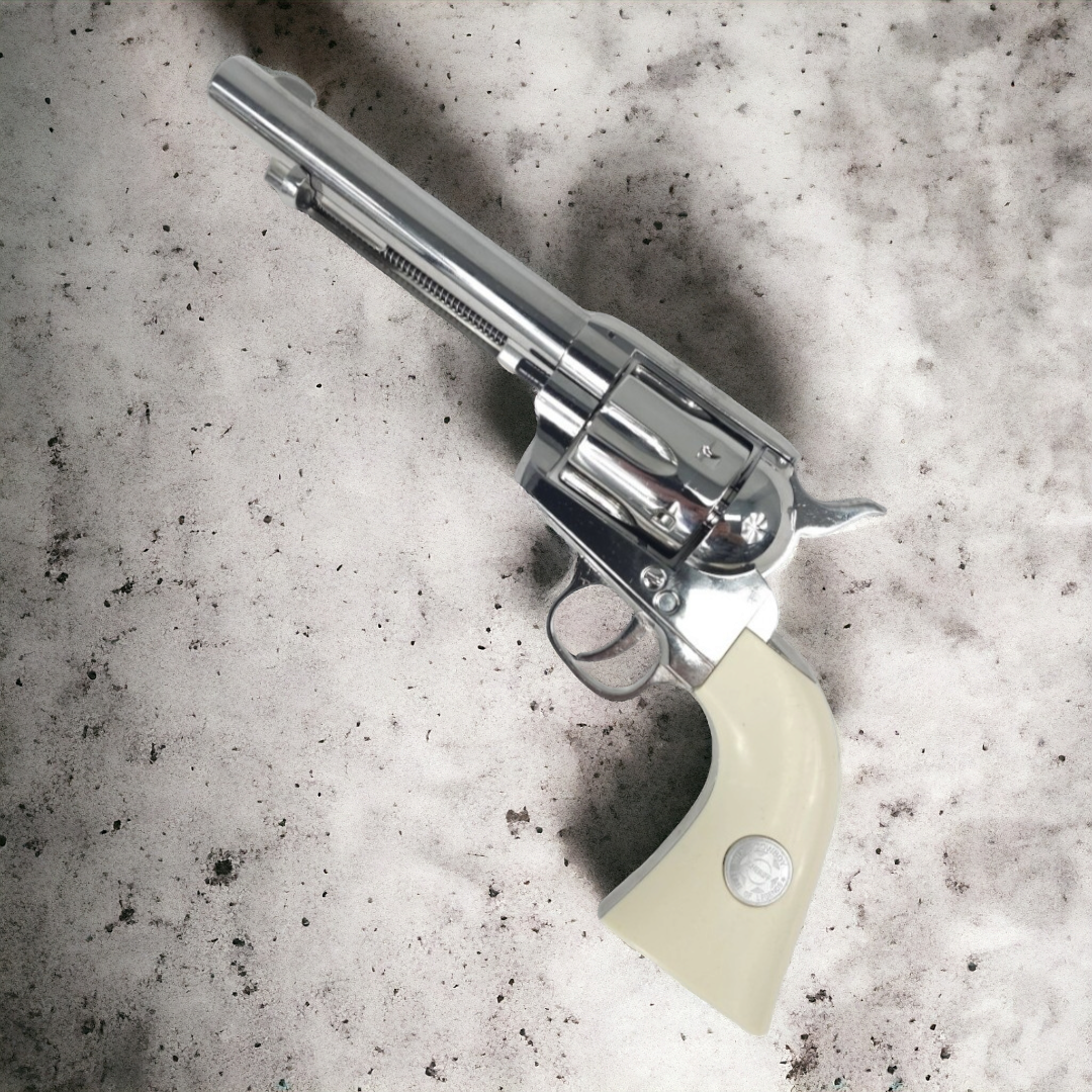 KELe Colt 1873 Peacemaker manual revolver with silver finish and ivory grip on a textured surface.